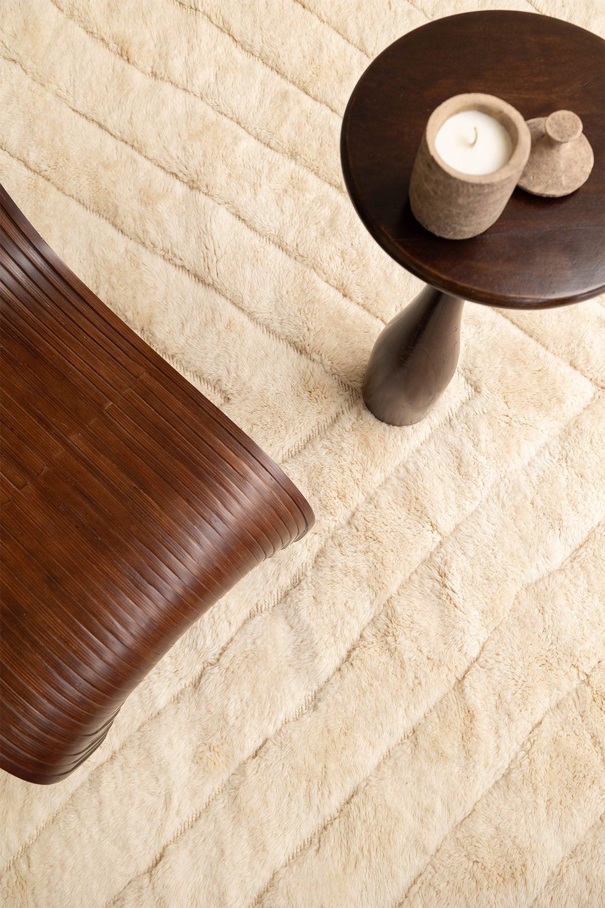 Elegant view of Barbary Wool's rug, highlighting its soft, plush texture and subtle linear design, paired with a curved wooden chair and a modern side table with earthy accents.