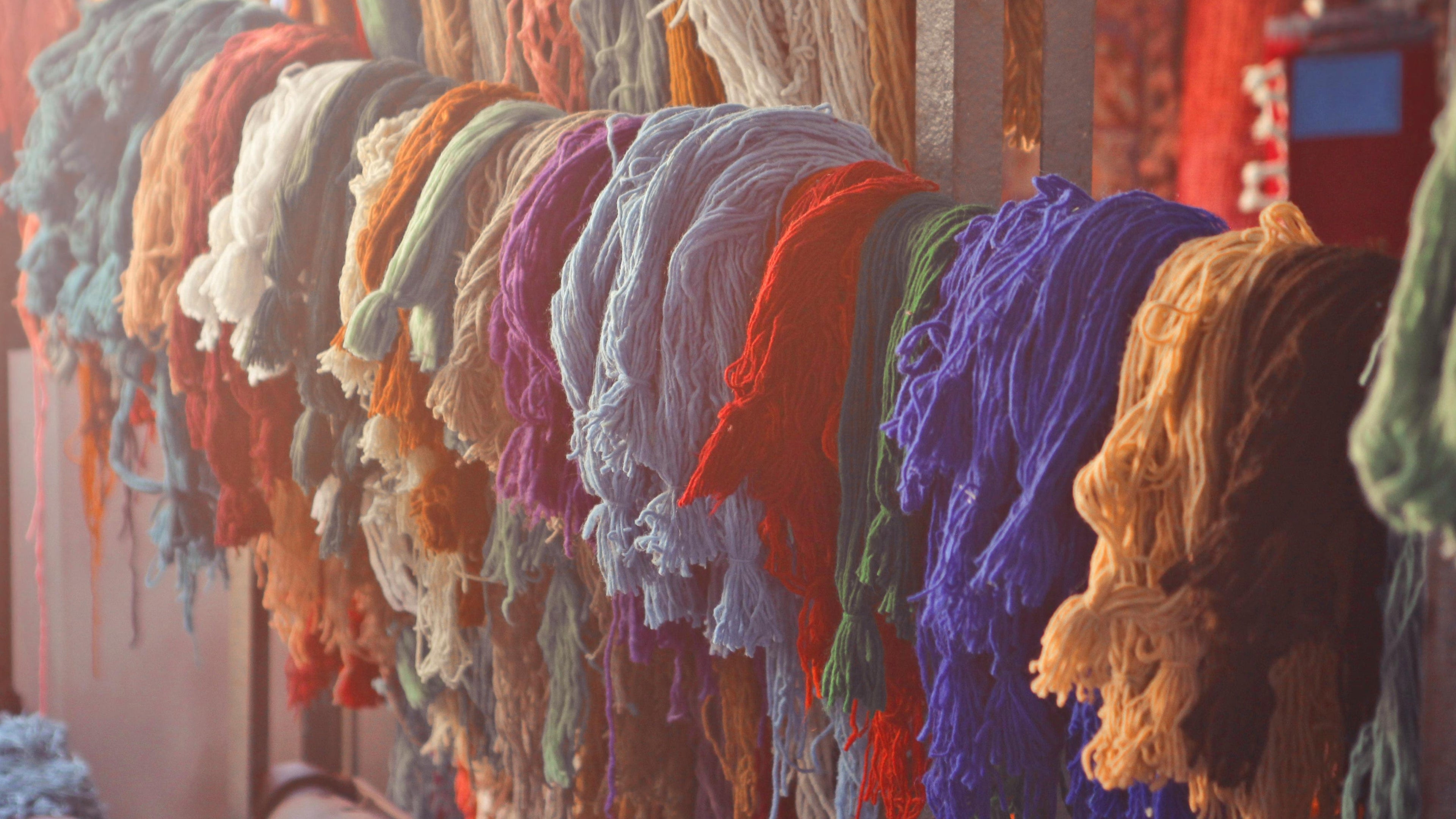 Colourful threads of wool hanging from a loom.